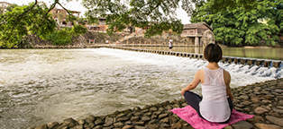 a woman meditating on a pink blanket looking out over moving water