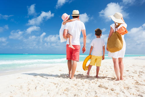Mother and father walking their two children on a white sandy beach
