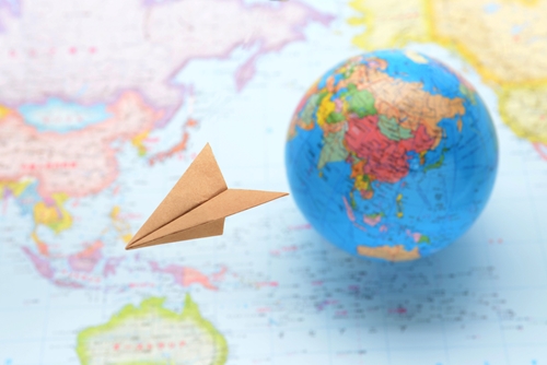 A globe sitting on a map behind a paper airplane