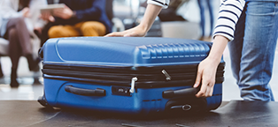 man or woman lifting blue suitcase off conveyor belt