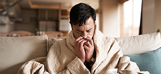Man wearing robe and sneezing into a tissue sick with the flu
