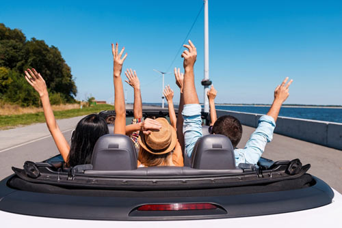people riding in a convertible car with arms raised