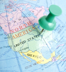 A section of a globe of North America with a green stick pin in the center of the United States